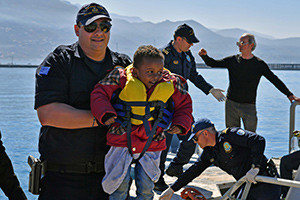A member of the Coast Guard carries a young refugee and other survivors off a rescue boat April 17 at the port of Kalamata, Greece. The survivors told U.N. staff that they had been part of a group of between 100 and 200 people who departed from Libya the previous week. (CNS photo/Nikitas Kotsiaris, EPA)