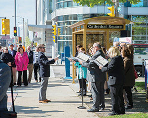 Christopher Berry, director of music at the Basilica of St. Josaphat, directs choir members at the May 18 unveiling of the bus stop at Jackson and Wells streets that is part of the basilica foundation’s attempt to raise $7.5 million for repairs to the Milwaukee landmark. (Catholic Herald photos by Peter Fenelon) 
