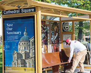 Jamie Jones from Above All Advertising installs a church pew in the bus stop at the corner of Jackson and Wells streets, Milwaukee, Wednesday, May 18. As part of the St. Josaphat Basilica Foundation’s effort to raise $7.5 million for external repairs to the historic church, the bus stop is designed to resemble the basilica. The bus shelter will be in place for 10 weeks. 