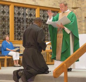 Salvatorian Fr. Joe Rodrigues, U.S. provincial and National Vocations Director, prays over Simon Muema, during Mass on Sunday, Aug. 14, when Muema made his first profession as a Salvatorian. (Catholic Herald photo by Peter Fenelon)