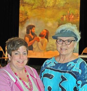 Amy Nelson, principal of St. John the Baptist School, Plymouth, and artist Kitty Lynne Klich pose in front of the image of the Baptism of Jesus that Klich painted to hang at the end of the school’s main hallway. (Catholic Herald photo by Sam Arendt)