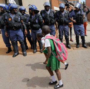 School children walk past a line of police officers during protests against the cost of higher education in Johannesburg, South Africa, Oct. 12. After chaos broke out in a Catholic church as it hosted a meeting to resolve a university crisis, South Africa’s Jesuits said the church would no longer be open for these talks. (CNS photo/Kim Ludbrook, EPA)