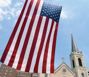 A 48-foot U.S. flag is seen June 24 outside Sacred Heart Church in downtown Peoria, Ill. In his Herald of Hope column, Archbishop Listecki suggests the church is under attack as a faith and a church by civil political forces. (CNS file photo/Tom Dermody, Catholic Post) 