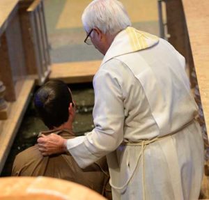 After immersing Andrew Landerholm in the baptismal font, Fr. Jeff Haines helps the newly-baptized Catholic out of the water.